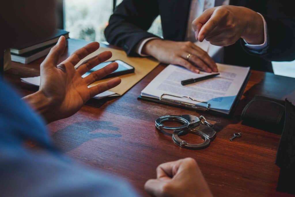 Criminal defense lawyer consulting client with legal documents and handcuffs on desk