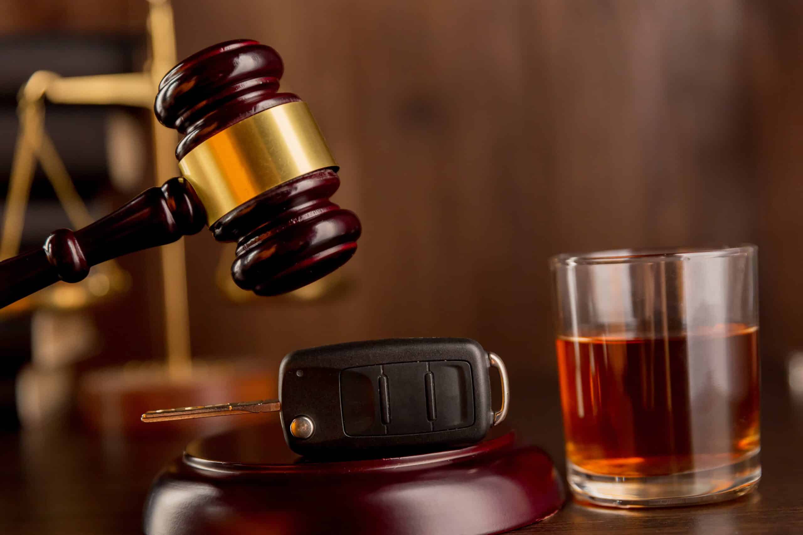 DUI law concept with judge’s gavel, car key, and glass of alcohol on courtroom desk.