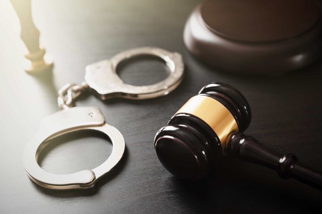 Judge’s gavel and handcuffs on courtroom desk symbolizing criminal defense and justice.