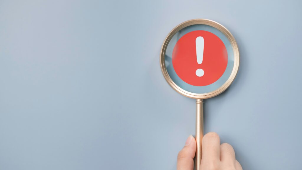 Magnifying glass highlighting red warning sign with exclamation mark on blue background