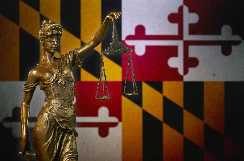 Lady Justice statue with scales of justice in front of Maryland state flag.