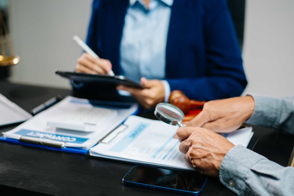 Lawyer reviewing legal documents with magnifying glass during client consultation at office